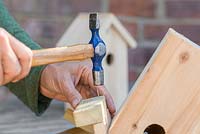 Secure the wooden batons to the roof of the bird house using a hammer