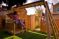 Girl on swing. Children's play area with wooden climbing frame. Small urban contemporary town garden. Ansari garden, Harrow