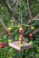 A Berry House bird feeder constructed from Bamboo, Wood, Conkers, Wire, String, Crab Apples, Sloe berries, Rose hips and Hawthorn berries. Bird tit feeding