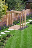 View of the Pergola in the middle of the path, surrounded by Buxus sempervirens cubes, Verbena bonariensis, Delphinium elatum 'Blaustrahl', Geranium 'Johnson's Blue' and Lavandula angustifolia 'Hidcote'