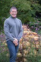 Garden designer Sean Butler of Cube 1994, standing beside a unique Gabion sculpture shaped like a bulb, with planting of Verbena bonariensis and Actaea