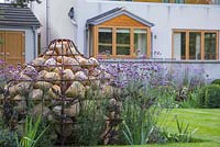 View of the house and unique Gabion sculpture shaped like a bulb, with planting of Verbena bonariensis and Actaea