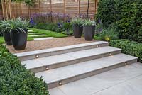 Marble steps with lighting feature at dusk. Verbena bonariensis and Calamagrostis x acutiflora 'Karl Foerster' in foreground and potted Astelia chathamica