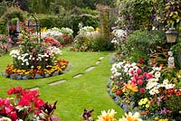 Colourful mixed beds filled shrubs, perennials and tender bedding plants, including Lobelia, Calendula Rosa Buddleia Clematis Achillea Leucanthemum Dahlia and Rosa with path across the lawn to pergola. Manvers Street, Derbyshire NGS August