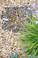 Homemade mosaic tile on gravel path in coastal garden 