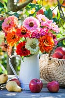 Jug of Zinnias and harvested fruits on the table.