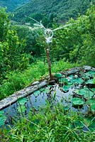 Lily pond with 'half bird, half insect - Guardian Des Sambucs' sculpture by Manu Rodriguez. 