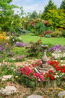 Colourful well tended garden belonging to plant enthusiasts. Gravel garden planted with rock plants, bedding plants, sundial, neatly mown lawn, collection of mixed ornamental shrubs and trees.