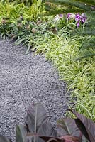 Gravel path leading past border planted with Ananas comosus 'Champaca' and Chlorophytum comosum 'Ocean'. The Hidden Beauty of Kranji. RHS Chelsea Flower Show, 2015.