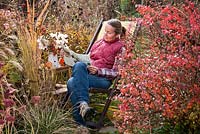 Woman relaxing on a deck chair reading garden magazine in autumn garden.