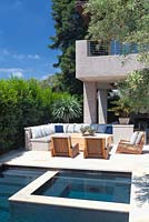 View of modern swimming pool with outside seating area sun loungers and mature olive tree.