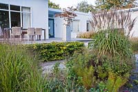 Border of perennials and grasses in October. Panicum virgatum 'Shenandoah', Miscanthus sinensis 'Malepartus'. Van de Voorde garden. Design: Tom de Witte