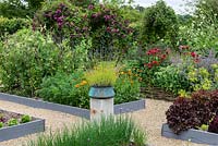 A potager with raised beds of vegetables and flowers including chives, salad leaves, peas, marigolds and bergamot. A stone plinth with a copper pot of lavender provides a focal point on the central axis.