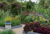 A potager with raised beds of vegetables and flowers including chives, salad leaves, peas, marigolds, lady's mantle, cephalarea and bergamot.