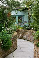 A tropical town garden with raised brick borders leading to a summer house.