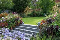 Stone steps leading to a lawn surrounded by colourful late summer borders and containers with perennials and succulents.