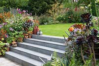 Stone steps leading to a lawn surrounded by colourful late summer borders and containers with perennials and succulents.