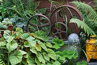 A decorative collection of metal industrial parts amongst begonia foliage and ferns.