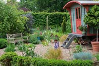 A painted wooden gypsy caravan in a gravel garden.