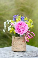 A colourful summer posy with pink rose, alchemilla, catmint, baby's breath and honeysuckle in a glass jar decorated with twine.