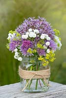 A summer posie with alliums, gypsophila and alchemilla in a glass gar decorated with twine.