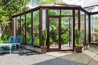 Conservatory that links the back of the house with a rocky outcrop behind it, with pond and border inside containing plants that would struggle to survive outside such as a tree fern, Dicksonia antarctica, Geraniums palmatum and aspidistras. Windy Hall, Windermere, Cumbria, UK
