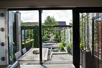 View to the garden from the house through the doors. Outdoor dining area, pond, decking, pergola. Family Fabry - Mathijs. Belgium