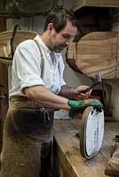 Charlie Groves making a traditional Sussex trug. After being steam bent, a length of sweet chesnut is bent round the former, a frame to create the trug handle. Behind, the Heath Robinson style steamer.