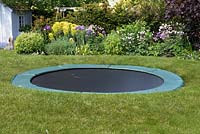 A trampoline set in a raised lawn so that from a distance it is largely concealed.