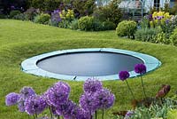 A trampoline set in a raised circle of lawn so that from a distance it is largely concealed.