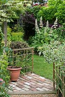 A brick path and cane fence leads to a corner planted with Rodgersia aesculifolia, Pittosporum 'Tom Thumb', euphorbia, wisteria and vitis.