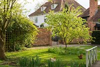 A 17th century farm house and country garden in spring, with chickens on the lawn beneath a tree.