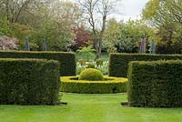 A formal garden room with circular box topiary and ball surrounded by yew hedges.
