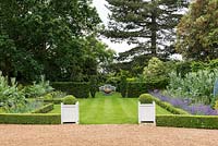 A view from Kelvedon Hall of a box edged formal lawn and herbaceous borders leading to a bench and Rugby ball sculture by Dominic Welch,