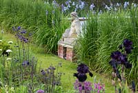A statue is flanked by blue siberian iris and feather reed grass, which hides the glass screen behind.