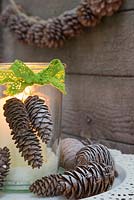 A candle jar decorated with a green laced bow and pine cones