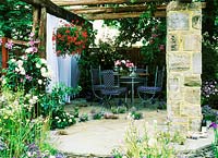 Patio with furniture, Hampton Court 2001, Design: Paul Dyer, the sound of the  countryside. Crazy paving patio with table and chairs, old timber pergola, geranium hanging basket, clematis, rosa and verbena  bonariensis