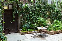 View of court yard with table and chairs to shelves with artefacts. Lucille Lewins, small office court yard garden in Chiltern street studios, London. Designed by Adam Woolcott and Jonathan Smith 