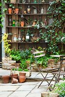 View of court yard with table and chairs to shelves with artefacts. Lucille Lewins, small office court yard garden in Chiltern street studios, London. Designed by Adam Woolcott and Jonathan Smith