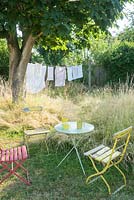 Wild garden with table and chairs under horse chestnut tree and washing drying on the line.