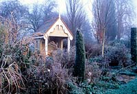 Garden in winter with hoar frost. Borders with garden building summerhouse. 