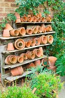Terracotta pots of different sizes stored neatly on a set of shelves outside. 