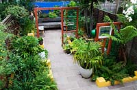 View from above showing exotic planting with Mexican feel, hard landscaping, dividing panels and seating made from sleepers. Green foliage shapes and texture - chusan palm in container and Dicksonia  - tree fern 