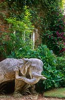 One of a pair of elephants framing the entrance to the South Court with Clematis 'Etoile Violette' climbing the gatehouse behind. Cranborne Manor Garden, Dorset