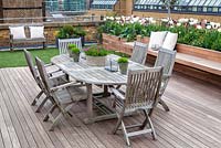 Dining table and chairs with faux lawn and raised beds planted with tulips and olive trees. April. 