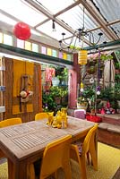 Inner city garden with begonias and spathiphyllums features colourful eclectic retro pieces sourced from local markets, including a timber dining setting with yellow chairs