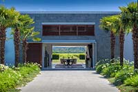 View along avenue of Trachycarpus wagernianus through the modern house to the vineyards beyond at Bhudevi Estate garden, Marlborough, New Zealand.