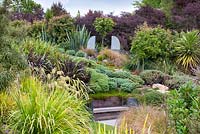 Selection of native Hebes, shrubs and grasses with antique statues at Bhudevi Estate garden, Marlborough, New Zealand.