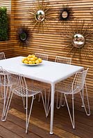 White aluminium chairs and table with porcelain enamelled steel top, french sixties sunburst mirrors on wall. Ben De Lisi House and Garden, London