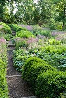 Paths edged with undulating hedges of clipped box lead down into the dell garden, awash with a matrix of planting including ferns, pink Silene dioica, orange euphorbia and Phlomis russeliana.